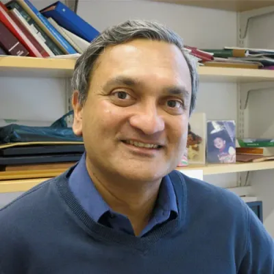 Mani Mahadevan headshot in an office witth a bookshelf in the background